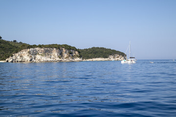 Sailboat and Dinghy in Serene Blue Waters by Rocky Coastline