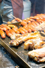 Juicy slices of grilled wild boar meat being roasted over open flames at a night market food stall. The smoky aroma and charred edges highlight the rustic and flavorful appeal of traditional street cu