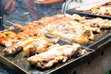 Juicy slices of grilled wild boar meat being roasted over open flames at a night market food stall. The smoky aroma and charred edges highlight the rustic and flavorful appeal of traditional street cu