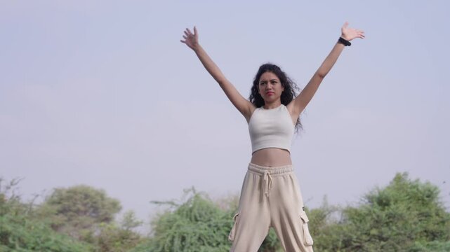  A slow-motion of South Asian young woman with curly hair training outdoors, with trees and sky behind her. Taken from low angle A slow-motion of South Asian young woman with curly hair training outdo