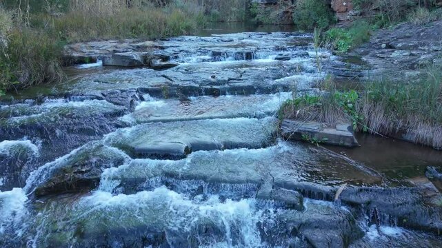 Marico Biosphere. A picturesque mountain stream gracefully cascading over rocky terrain, surrounded by vibrant lush vegetation.