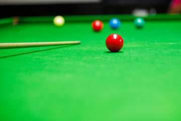 Close-up of red snooker ball on green table with cue in background. Concept of precision, sport, competition, and concentration in snooker or billiards.