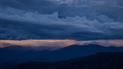 Stunning mountain landscape at sunset with dark storm clouds and golden light breaking through. Perfect for themes of nature, weather, and outdoor beauty.