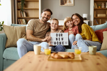 Happy  parents and their kids holding announcement message that this is their first home. They are...