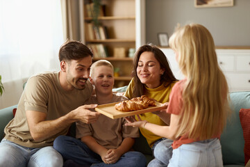 Happy  family enjoying in their time at home while daughter is bringing croissants to her parents...