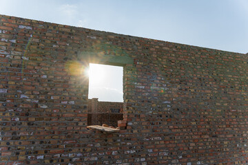Bright sunlight shines through an unfinished window opening in a newly constructed brick wall on a...