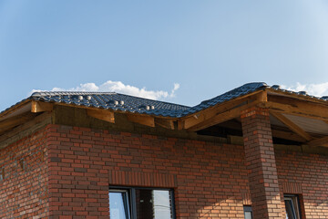 A brick house nears completion with a newly installed roof under a bright sky, showcasing the...