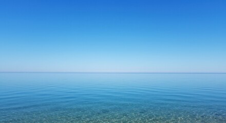 Obraz premium A serene seascape featuring calm, clear blue water meeting a cloudless, vibrant blue sky.