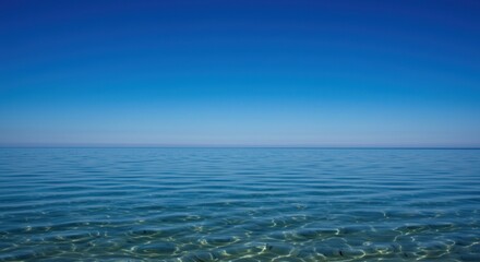 A serene seascape featuring calm, clear blue water meeting a cloudless, vibrant blue sky.