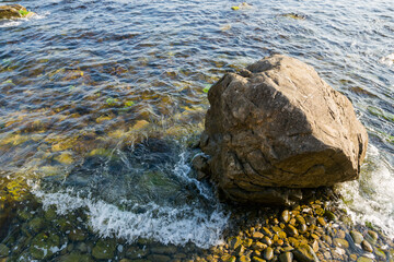 huge rock on the pebble sea shore. transparent calm water with seaweed near the coast. summer vacation at the beach on a sunny morning