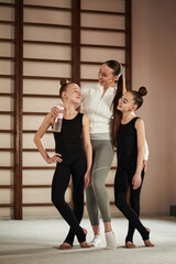 Caucasian young adult woman coaching two Caucasian girls during rhythmic gymnastics training, all...