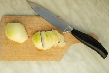 Sliced onion on a wooden cutting board with a kitchen knife placed beside it.