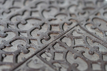 Close-up view of a decorative metal gratepanel with stylized floral patterns in warm, golden light against dark background.