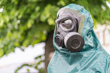 Person in protective gear, green plasticrubber suit with ventilation holes, hood, goggles, dark...