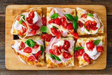 Pinsa Romana with boiled ham, burrata cheese, basil leaves and cherry tomatoes on wooden table	