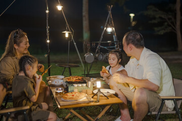 A family of four is sitting around a table eating pizza. A man is sitting on the right side of the...