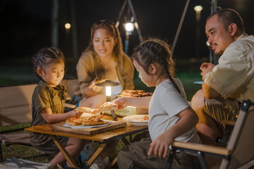 A family of four is sitting around a table with pizza and a lantern. A young girl is sitting in the middle of the table