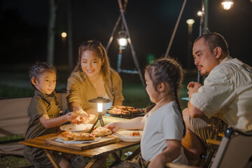 A family of four is sitting around a table with pizza. A man is sitting on a chair next to a woman and two children