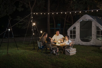 A family is sitting around a table in a backyard. There are three people, two of whom are women and one is a man. They are eating food and enjoying each other's company