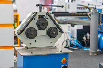 Image presents an indoor industrial setting, featuring a CNC machine or lathe with gray metallic components and controls The background contains additional machinery, possibly tanks No visible cont