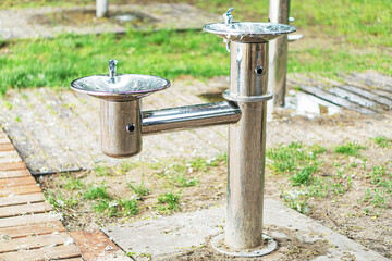 Outdoor public drinking fountain, metal construction, two spigots, small basins, silver paint,...