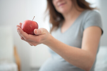 Expecting mother holding fresh apple while gently caressing her baby bump. Peaceful moment of...