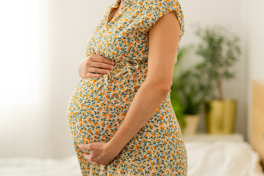 Close-up of expecting mother gently stroking her rounded belly in peaceful home setting. Tender moment of maternal connection and anticipation.