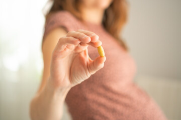 Expecting mother holding medicine pill while touching her belly. Careful health management during pregnancy following doctor's recommendations.