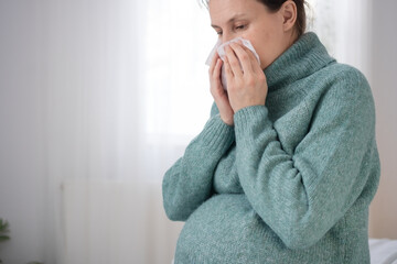 Expecting mother using tissue while having cold during pregnancy. Caring for health while experiencing common illness at home.