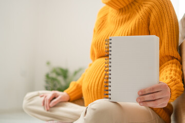 Empty notebook in hands of expecting mother, waiting to be filled with important pregnancy notes and hospital checklists. Cozy home preparation.