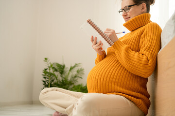 Expecting mother writing essential items list for maternity hospital in cozy home setting. Organized preparation for upcoming delivery and baby arrival.