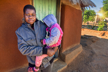 African village, single mother with child , holding toddler standing in front of the house in the...