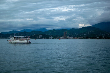 Passenger Ferry with Red Stripes Crossing Coastal Waters under Clouded Sky