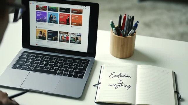 Laptop shows web thumbnails execution motto on notebook with pens in a wooden holder on a white desk