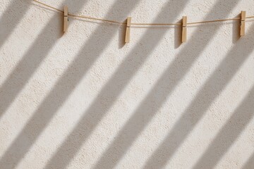 Diagonal shadows of clothespins on beige wall in sunlight