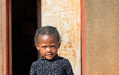 African village, single child girl with braids , toddler standing in front of the house in the...