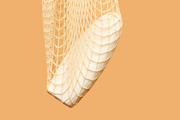 White shampoo container in white eco-net. On beige background.