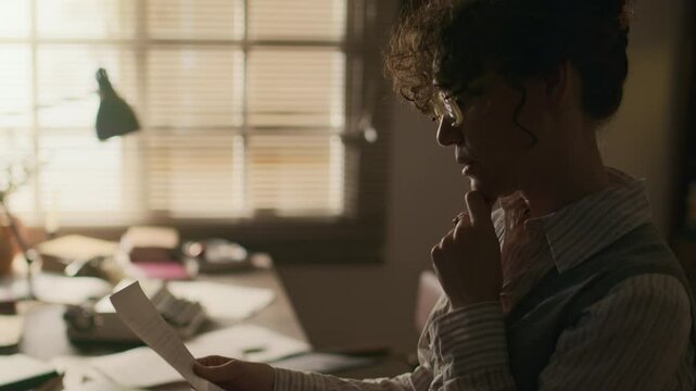 Side view shot of focused middle-aged Caucasian female journalist or writer in retro outfit and eyeglasses working on manuscript for new publication in study room