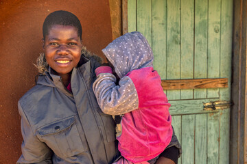 African village, single mother with child , holding toddler standing in front of the house in the...