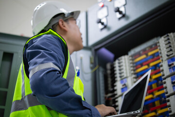 Engineer in safety vest and helmet performs load inspection at electrical unit center using laptop...