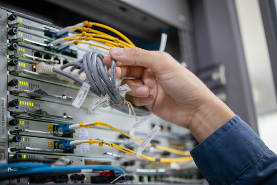 Network technician performs careful inspection of LAN patchpanel connecting multiple cables to ensure proper data flow and system functionality in server room environment - Powered by Adobe