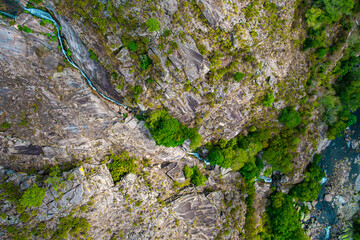 A top-down shot of a rocky canyon with a thin stream flowing through it and patches of green trees...