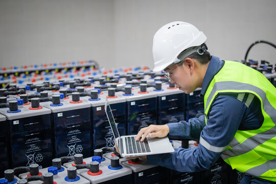 Technician inspects backup battery power system using laptop in industrial setting ensuring system operates efficiently and safely with focused attention and care