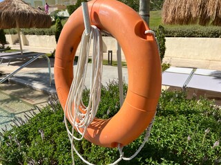 An orange lifebuoy hangs on a pole in front of a swimming pool. Symbol of safety and rescue...