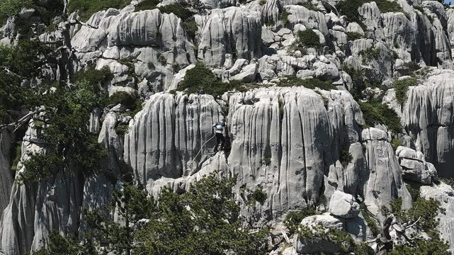 Drone view of professional rock climber ascending steep grey rock face demonstrating technical skill and safety in rugged mountain terrain, Tresteni vrh, Montenegro