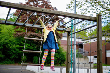 Little girl doing gymnastics on a climbing frame, horizontal bar on school yard. Child enjoying...