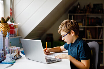 Kid boy with glasses learning at home on laptop for school. Adorable child making homework and...