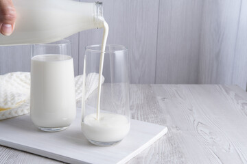 Pouring homemade kefir, buttermilk or yogurt with probiotics. Yogurt flowing from glass bottle on light background. Probiotic cold fermented dairy drink. Trendy food and drink. Copy space