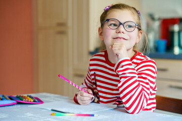 Little girl with eye glasses writing with pencil. Happy child doing elementary school homework....