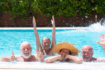 A group of four seniors, carefree and happy, smiling by the pool, enjoying their vacation or...